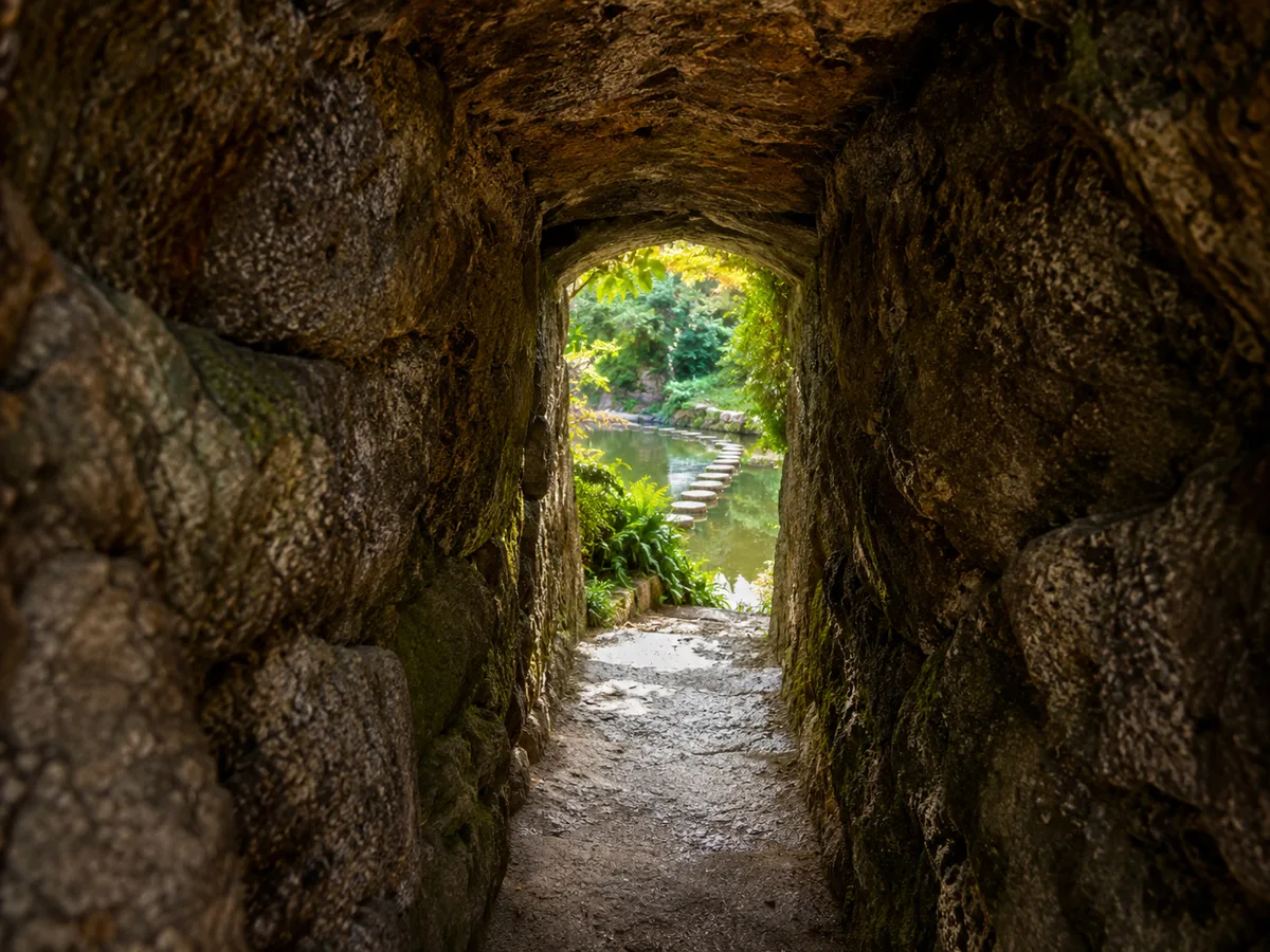 A rough granite tunnel at Quinta da Regaleira opening onto a green garden
